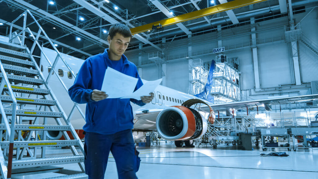 Foto Ingenieur / Flugzeugmechanikers in einer Wartungshalle vor einem Flugzeug als Beispiel für Stelle technischen Berufe / Luftfahrttechnik wie auch Produktion, Logistik, IT, Marketing, Verwaltung und weitere.
